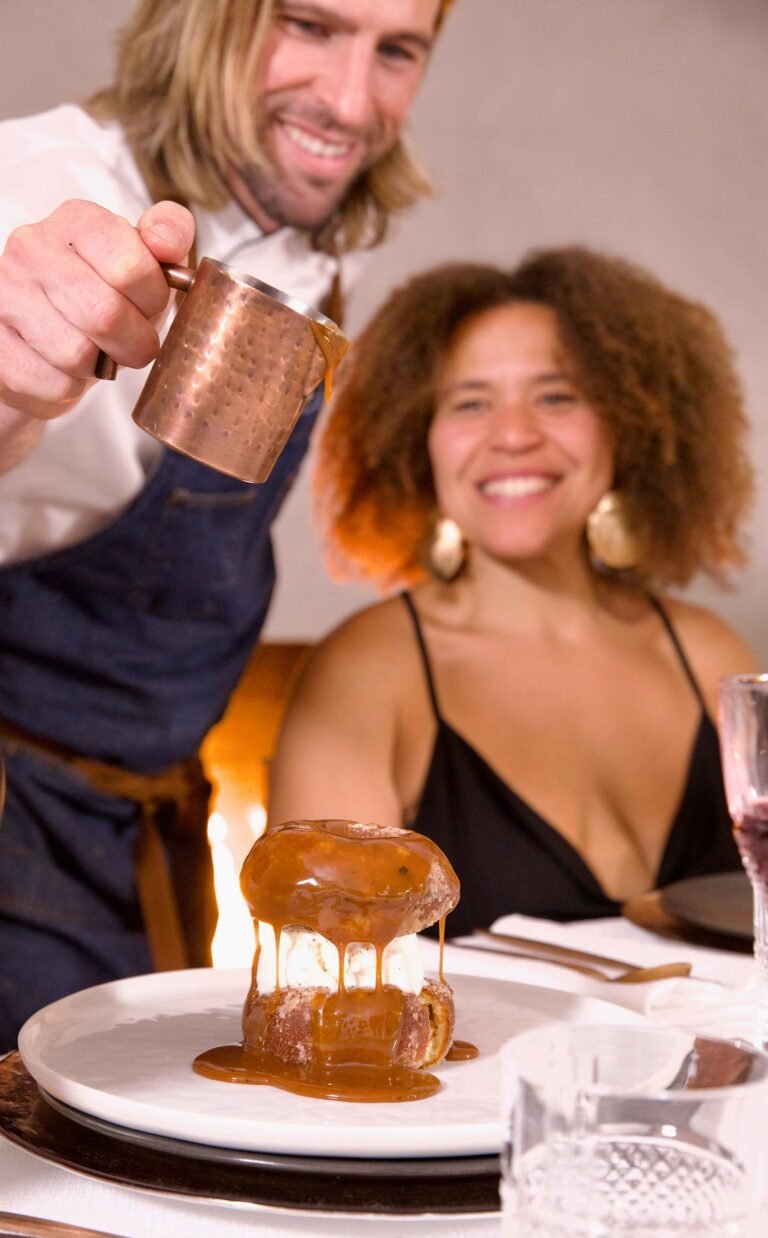 Chef Trevor Ross pours sauce over dessert and woman smiles